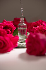 Clear glass bottle filled with oil is placed on a soft surface. A dropper releases a single drop of...