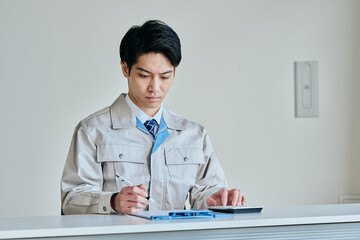電卓で計算する作業服姿の若い男性