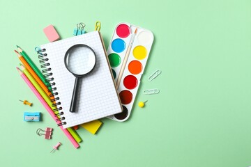 Colorful arrangement of school supplies including paints, pencils, notebook and magnifying glass on...