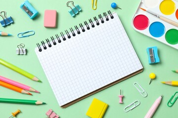 Collection of school supplies including notebook, pencils and stationery on green background