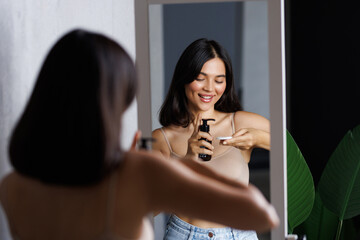 Beautiful woman taking care of skin by applying moisturizer cream in bathroom
