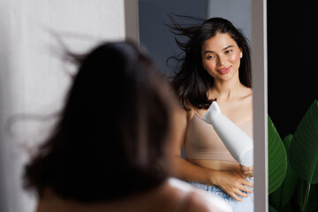 Beautiful woman using hair dryer near mirror at home