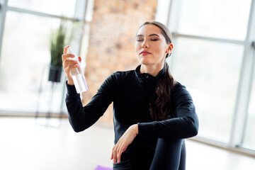 Charming woman enjoying a relaxing moment during her sports practice at home using spray for a...