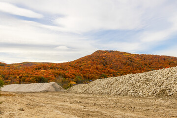 large mounds of limestone rubble on the background of a hill with a colorful autumn forest