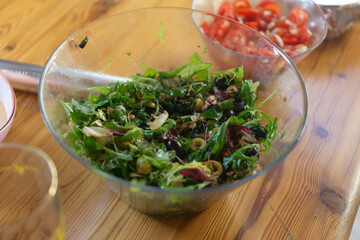 a large bowl of fresh salad with mixed greens, olives, and onions, on a wooden table with a side of chopped tomatoes, concept of food, healthy eating, cooking