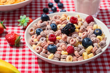 Close up of colorful cereal loops topped with fresh blueberries, raspberries, and blackberry in a bowl on red checkered tablecloth, highlighting healthy breakfast and vibrant texture