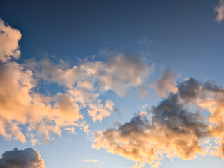 Warm golden hour sunlight illuminates fluffy cumulus clouds, drifting serenely across a vast and clear blue sky during a beautiful sunset.