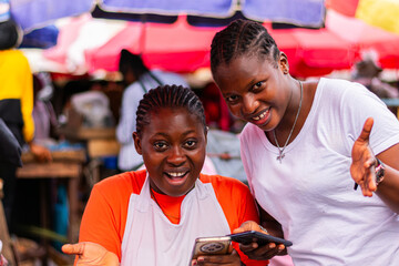 Young, happy African market woman and her customer holding smartphones, overly excited