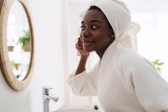 Smiling woman wearing bathrobe looking in mirror at home
