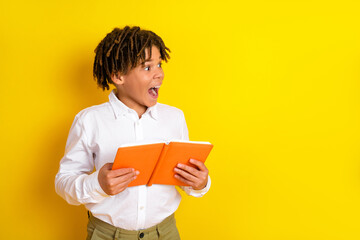 Energetic schoolboy surprised with an orange book against a vibrant yellow background expressing...