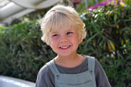 Smiling blond little boy portrait outdoors in summer greenery