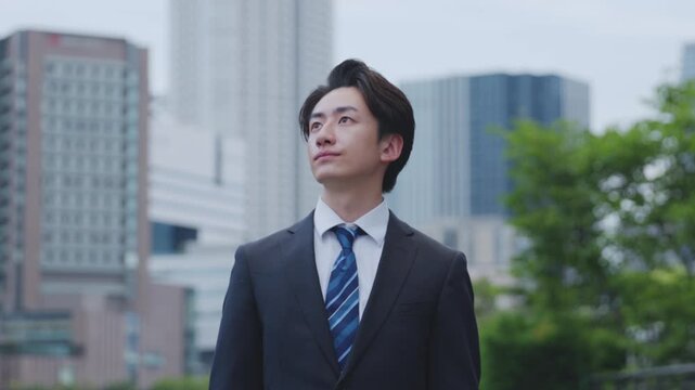 ビルを背景に遠くを見つめるスーツを着た日本人ビジネスマンの男性	