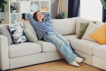 Young woman relaxing on a comfortable sofa at home while enjoying daylight during a cozy weekend...