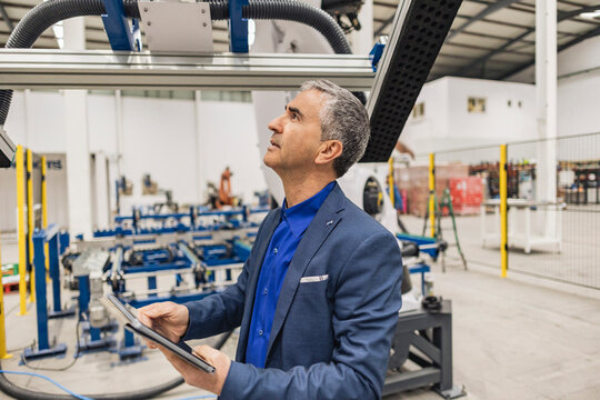 Mature businessman with tablet PC examining robotic arm in factory