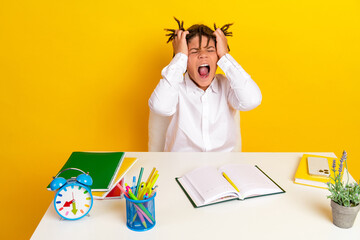 Frustrated schoolboy with homework at desk and yellow background, showcasing childhood education...