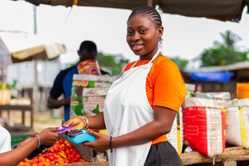 Young, excited African market woman collecting POS payment from a customer