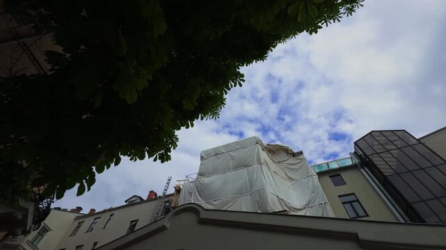 A construction site prominently features a very large white tarpaulin spread out under an overcast sky above