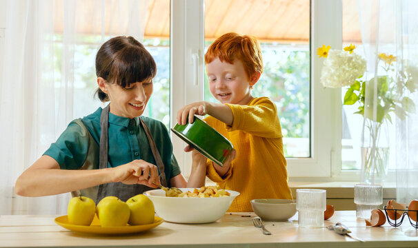 Redhead boy helping mother cooking food in kitchen at home