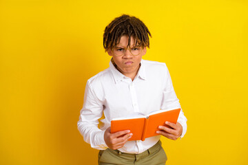 Portrait of a young boy in a white shirt holding a book with a yellow background, showcasing an...