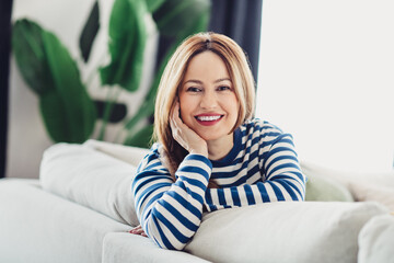 Beautiful woman in a striped sweatshirt relaxing on a comfortable sofa at home, surrounded by...