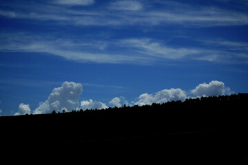 line of convective clouds popping up behind a silhouette of a mountain slope in dark blue sky
