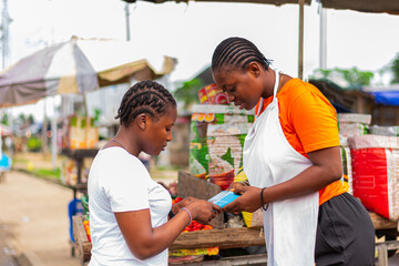 Young, excited African market woman collecting POS payment from a customer