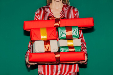 Woman in red pajamas holding stack of Christmas gifts indoors