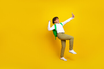 Energetic young schoolboy taking a selfie with excitement against a vibrant yellow background