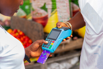 Young, excited African market woman collecting POS payment from a customer