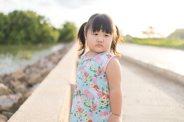 A cute little Asian girl is walking in a park in the evening,Asian baby child little girl walking on the street in the evening around the house. She holding the two finger and look  at the photographe