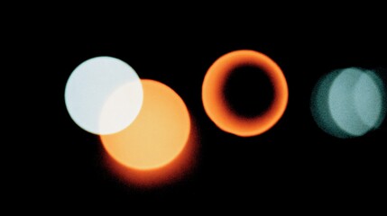 Abstract bokeh four luminous orbs, white, orange, and teal, on black