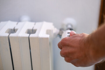 man regulates temperature in house with thermostat on white radiator, close-up male hand, saving...