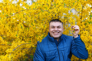 portrait of a man on the background of yellow forsythia flowers, spring nature and blossoms