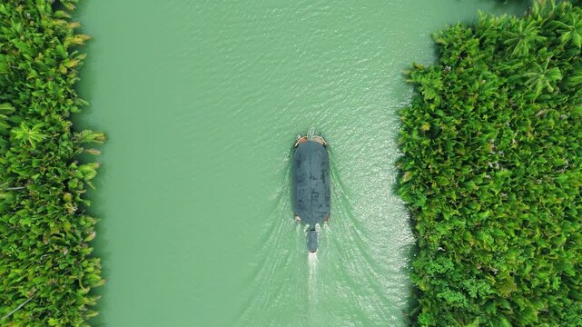 Aerial shot of a boat on a green river, surrounded by dense tropical foliage, in the Amazon rainforest.