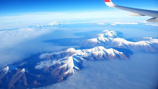 An aerial view shows a plane wing, snow capped mountains, lakes, and a clear blue sky.