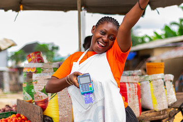 Young, excited African market woman holding POS machine with a debit card