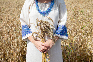 Woman in a field of winter wheat: Happy girl with a bouquet of wheat ears in traditional clothes...