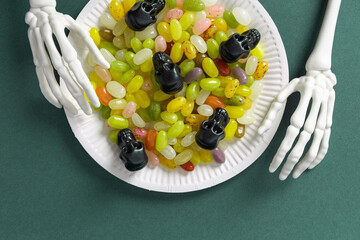 Skeleton hands holding plate of colorful jelly beans and black small decorative skulls