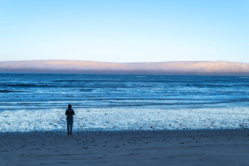 A person stands on an empty beach looking at the Pacific Ocean.