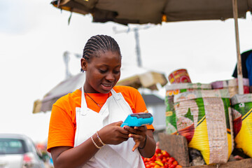 Young, excited African market woman holding POS machine with a debit card