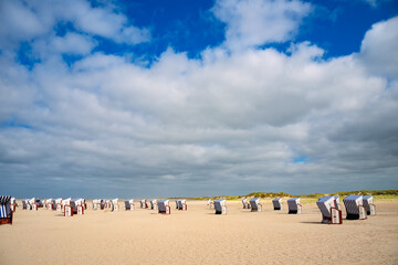 Blue and white striped beach chairs on sandy beach of the North Sea island of Norderney in Wadden Sea National Park invite you to sunbathe. Panoramic wide angle view of German dream destination.