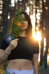 A young woman holding a fern leaf in her hands, with her face gently lit by the warm glow of the...