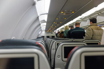 Travelers prepare to board a flight inside the airplane cabin with empty seats in view. The...