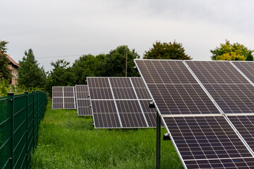 Solar energy farm with photovoltaic panels arranged on green meadow near residential area with...