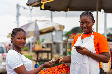 Young, excited African market woman collecting cash payment from a customer