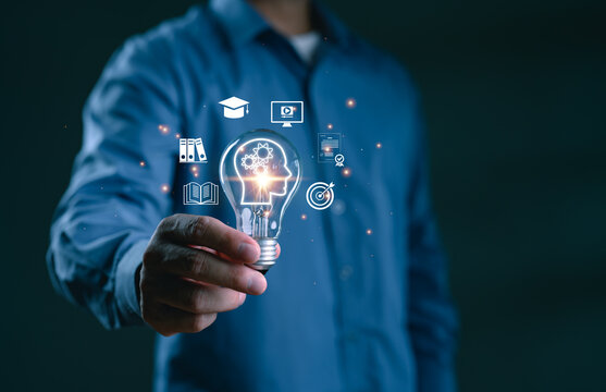 Businessman holding light bulb with learning and education icons. Concept of knowledge development, digital education, innovative learning, brain training, online course and future skills.