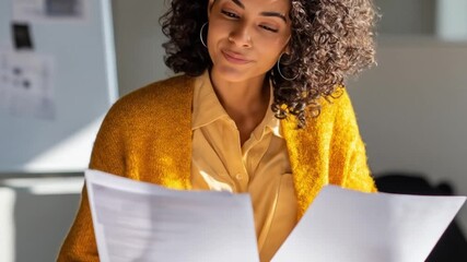 A focused woman in a bright yellow cardigan reads documents in a sunlit office setting.