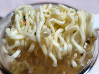 Rolls of springy white instant noodles are lifted with a spoon from the bowl, highlighting their...