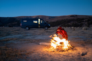 A woman aged around 35 standing next to a bonfire at sunset