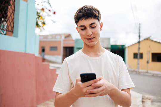 Teenage boy with braces using smartphone outdoors in colorful neighborhood